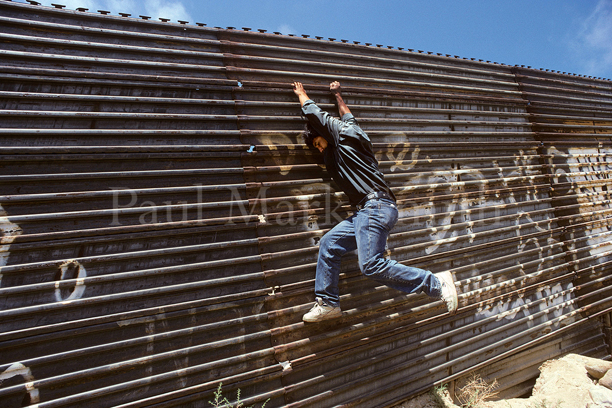 A migrant scales the border fence between Tijuana and San Diego.